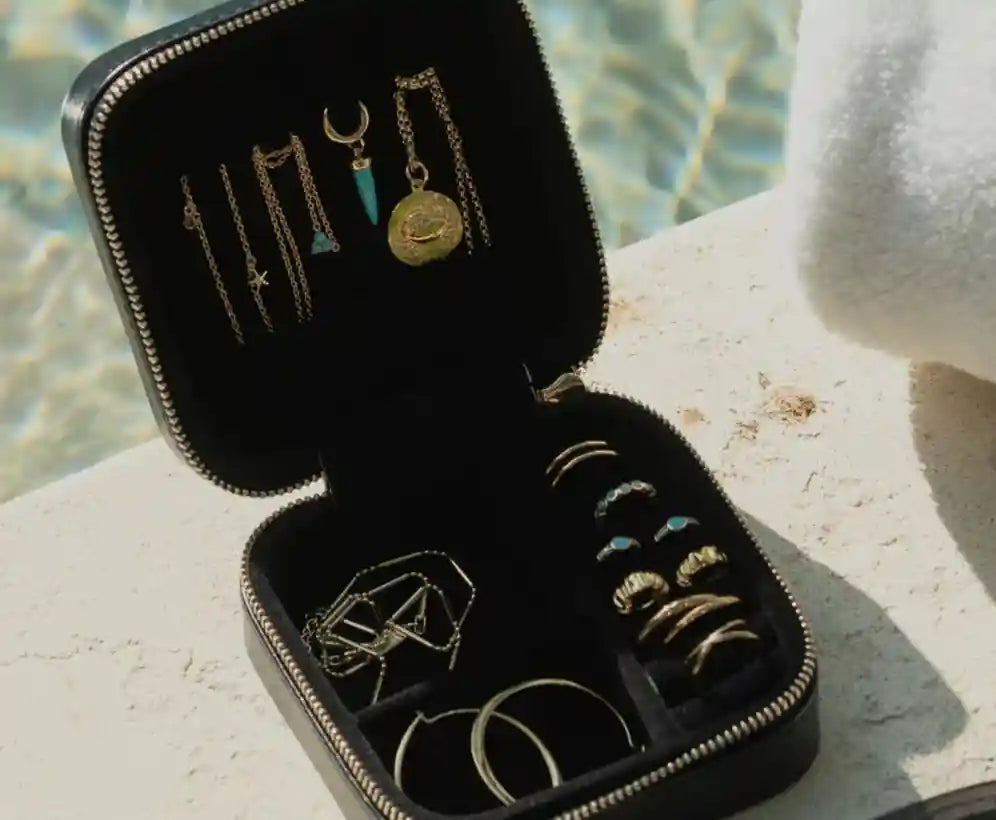 Black jewelry case with necklaces and rings on a stone surface with water in the background